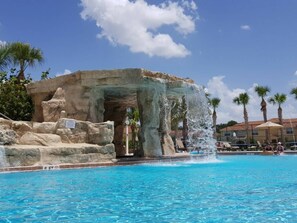 Ein Pool mit Wasserfall, umgeben von Palmen und einer Steinstruktur.