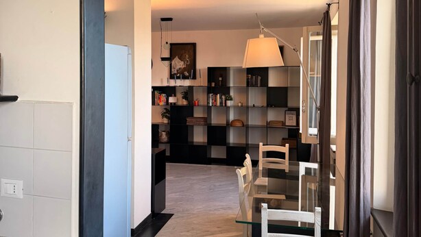 A modern kitchen with a dining area, featuring a central island, a chandelier, and a bookshelf. - Vista Mare Antico [Mura delle Grazie] (Genoa)