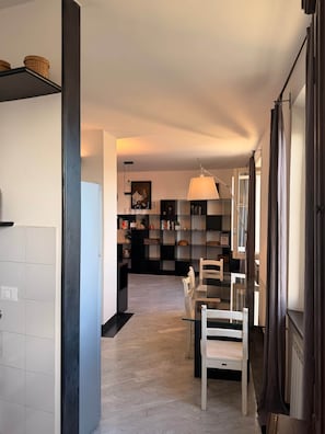 A modern kitchen with a dining area, featuring a central island, a chandelier, and a bookshelf.