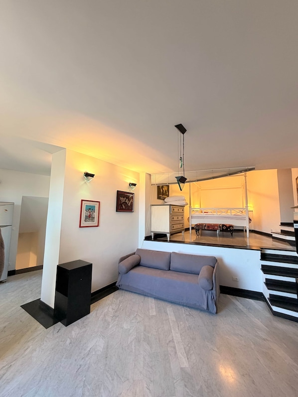A modern living room with a sofa, a black speaker, and a staircase leading to a bedroom.