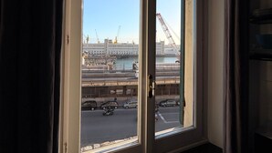 A window with a view of a busy street and construction cranes. - Vista Mare Antico [Mura delle Grazie] (Genoa)