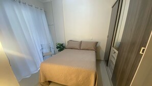 A bedroom with a bed, a chair, a plant, and a wardrobe.