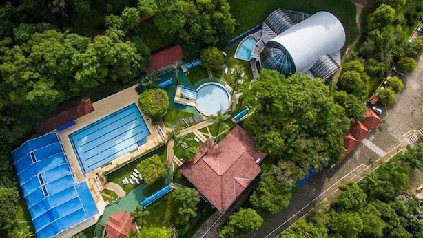 An aerial view of a resort with a large swimming pool, a dome-shaped building, and lush greenery.