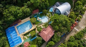 Ett flygbildsbild av ett semesterområde med en stor swimmingpool, en kupolformad byggnad och frodig grönska.