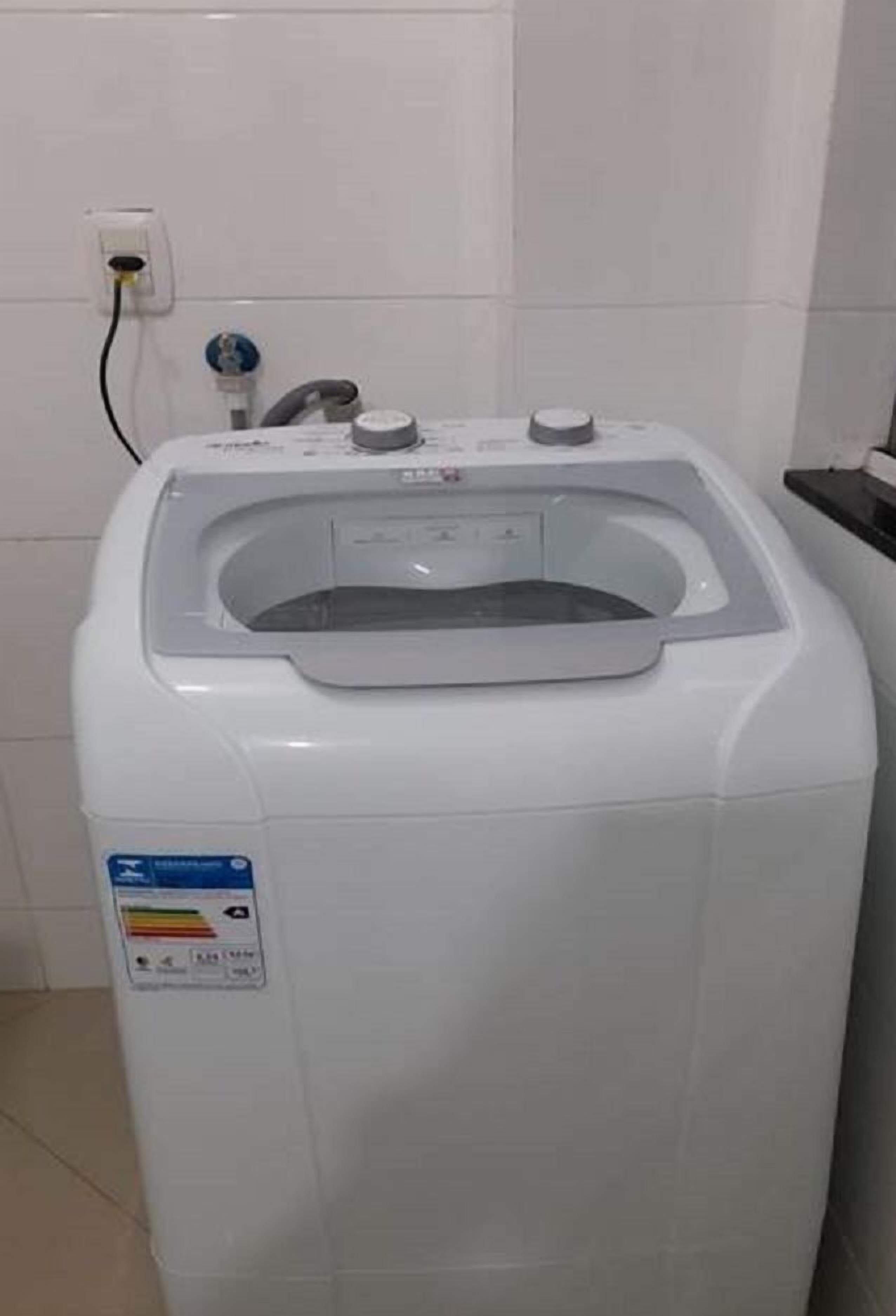 Eine Waschmaschine mit Frontlader in einem Badezimmer mit weiß gefliesten Wänden und einer sichtbaren Steckdose.