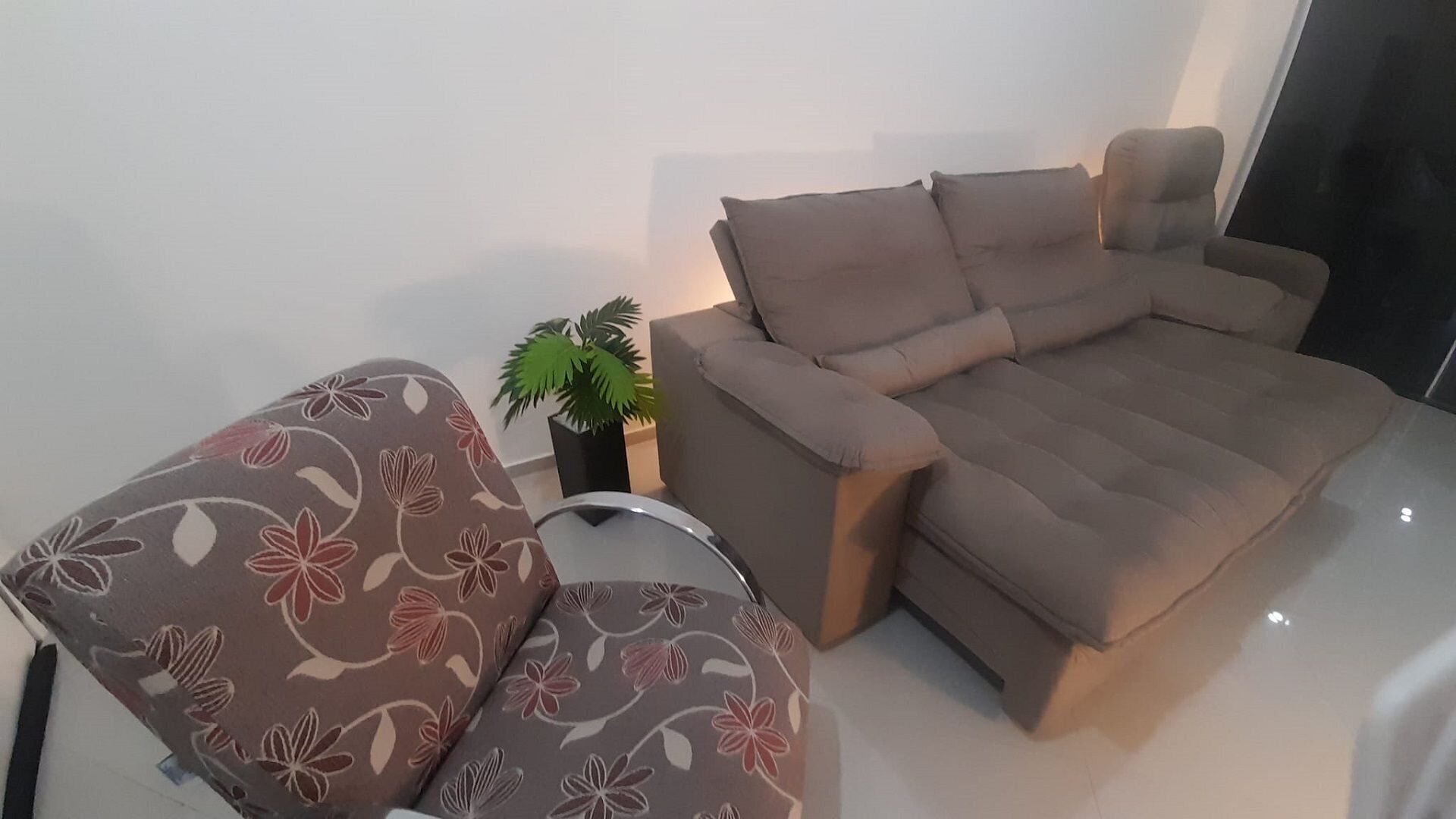 A modern living room with a sofa and a chair, a small potted plant, and a glass table.