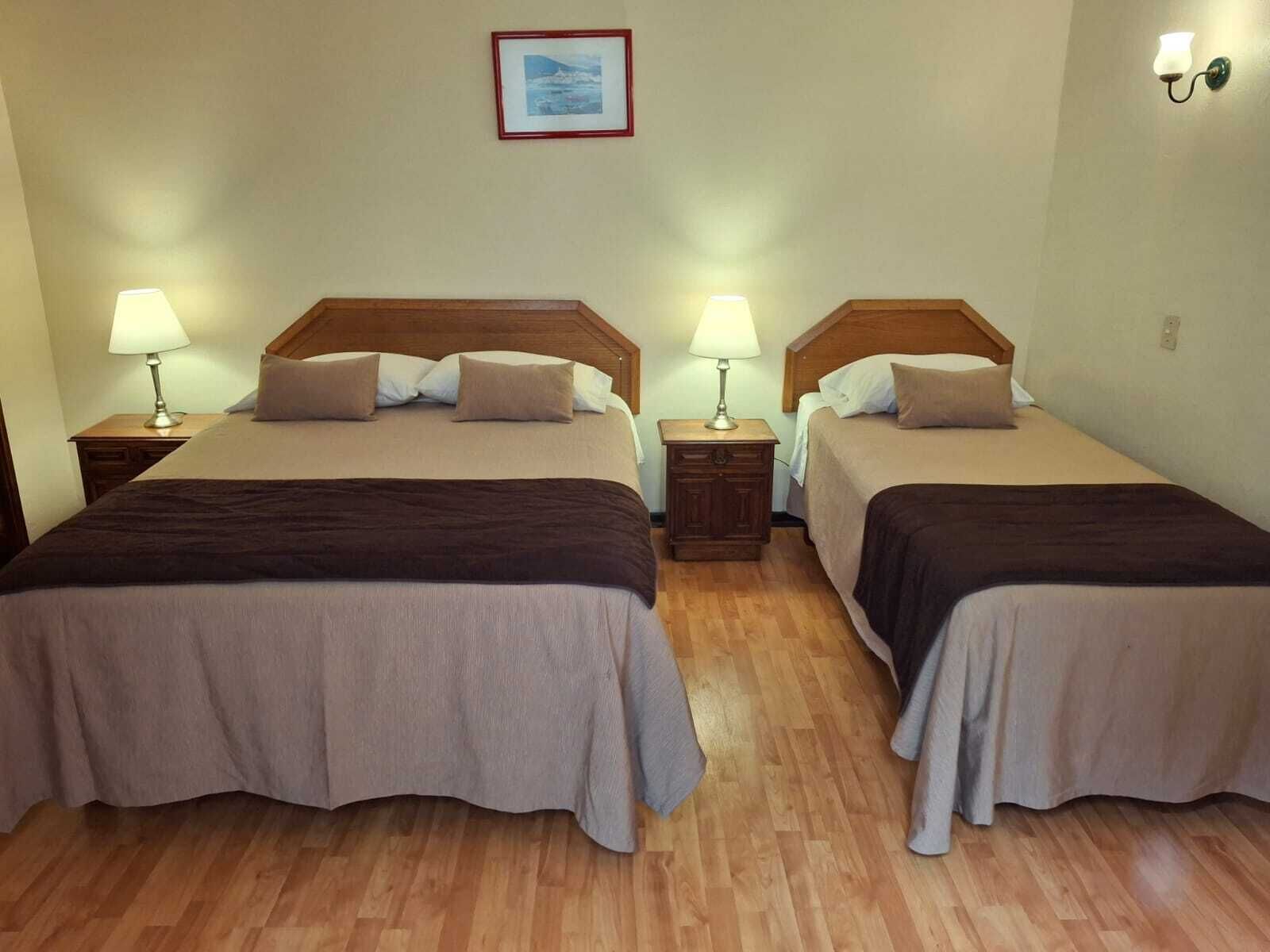 A double room with two beds, each with a wooden headboard, a bedside table, and a lamp.