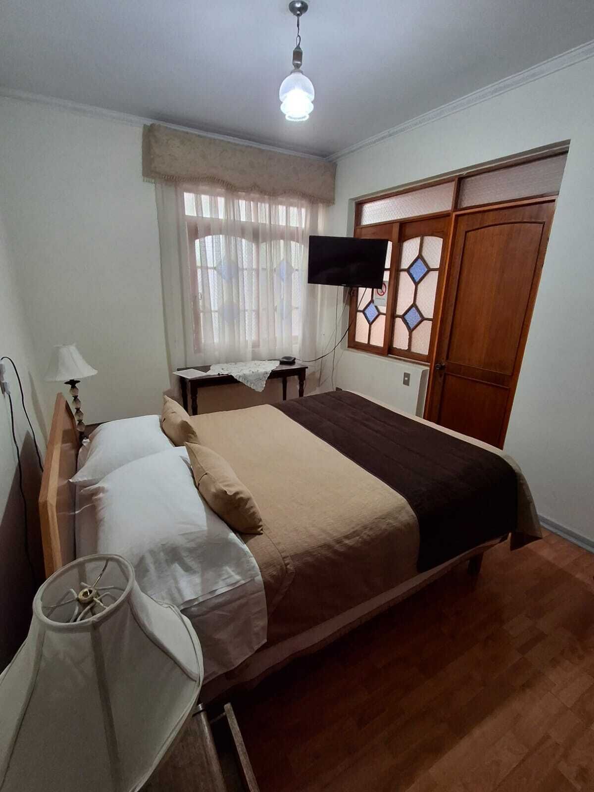 Een slaapkamer met een bed, nachtkastje, lamp, televisie en een garderobe.