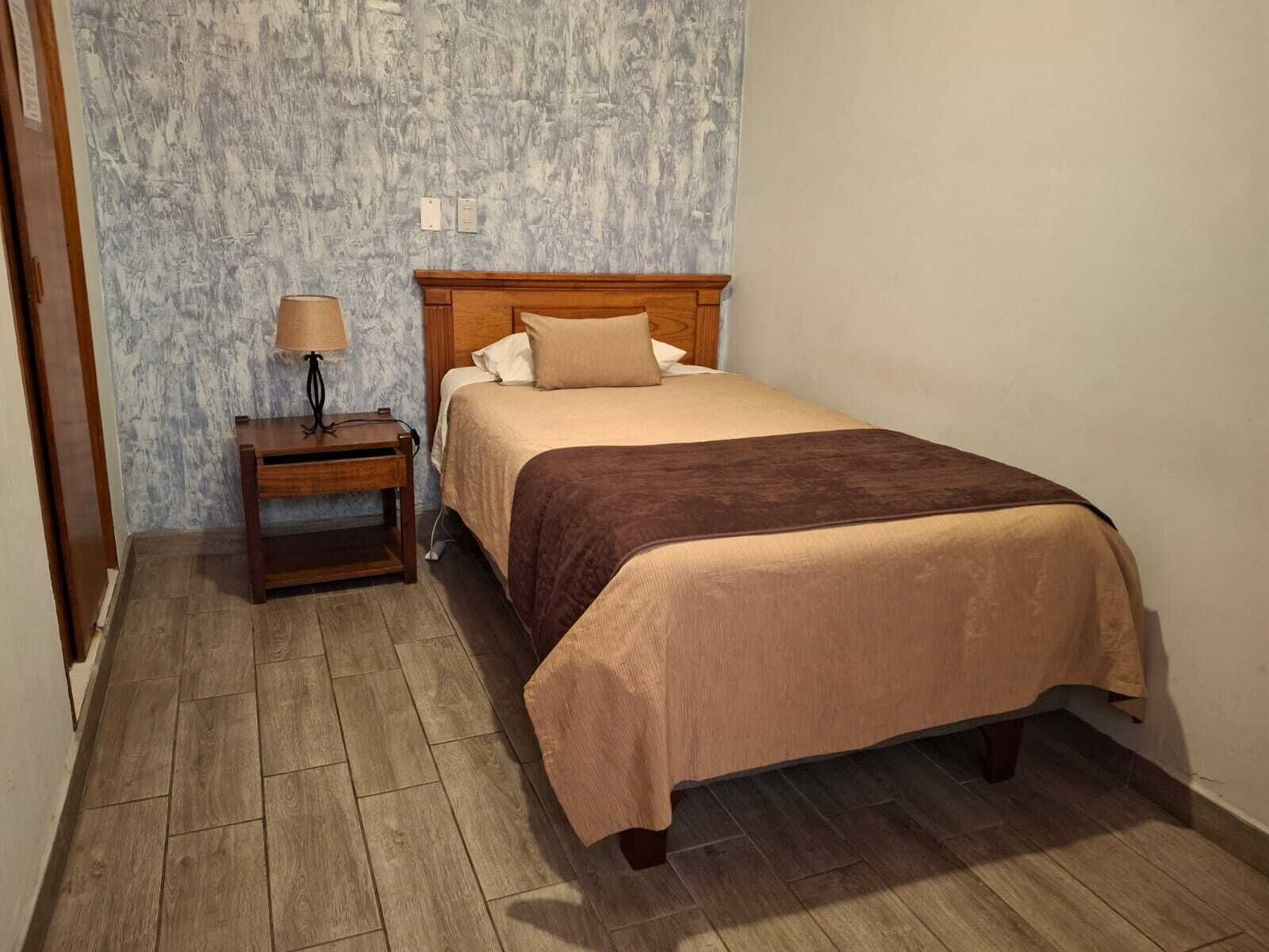 A neatly arranged bedroom with a wooden bed, a bedside table with a lamp, and a textured wall.