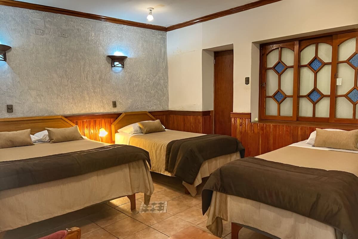 A hotel room with three single beds, wooden headboards, a tiled floor, and a decorative window with blue glass panes.