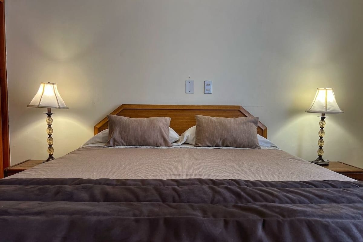 A neatly made bed with a wooden headboard, two bedside lamps, and two electrical outlets on the wall.