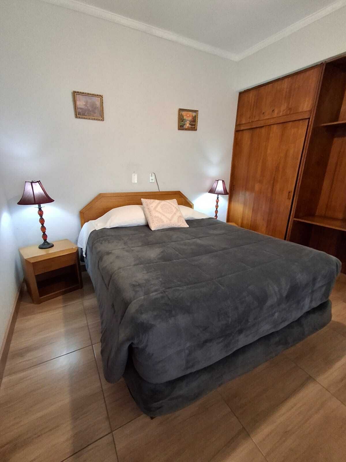 A bedroom with a large bed, wooden wardrobe, two bedside tables with lamps, and two wall-mounted picture frames.