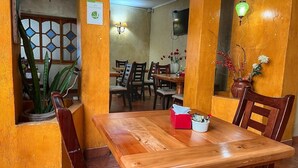 Un coin repas avec une table et des chaises en bois, une boîte à mouchoirs rouge et un vase avec des fleurs.