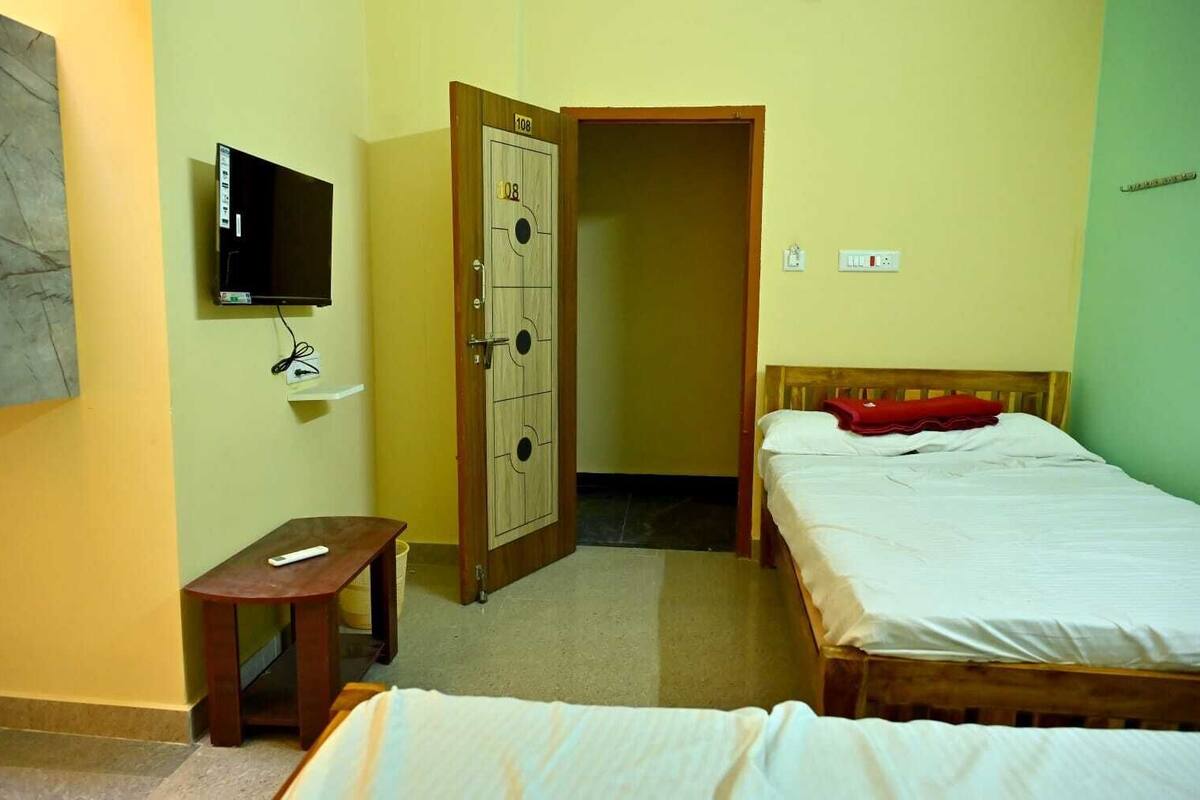 Un dormitorio con dos camas, un televisor montado en la pared, un armario de madera y una mesita.