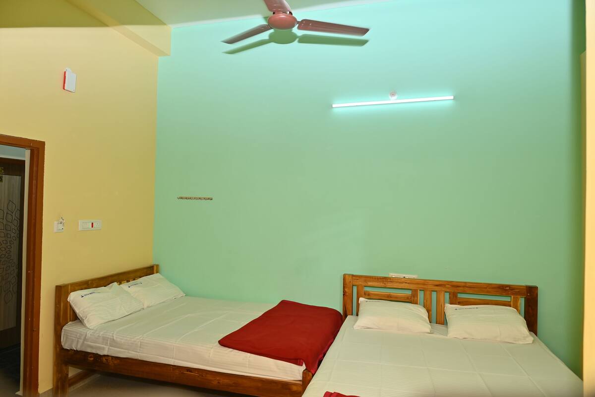 Una habitación con dos camas individuales, un ventilador de techo y una lámpara fijada a la pared.