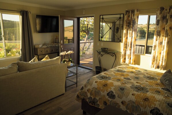 A bedroom with a bed, a sofa, a TV, a balcony with a view, and a dining area with a table and chairs.