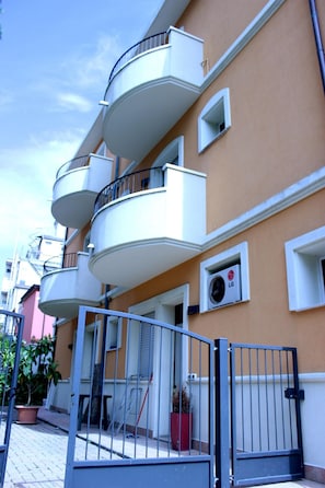 A multi-story residential building with balconies, a gated entrance, and a small air conditioning unit on the wall.