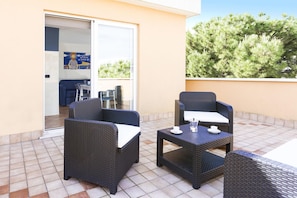 A balcony with wicker furniture, a glass door leading inside, and a view of trees.