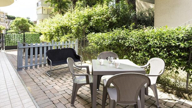 An outdoor patio with a table and chairs, a covered seating area, and a hedge in the background.
