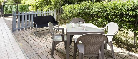 An outdoor patio with a table and chairs, a covered seating area, and a hedge in the background.