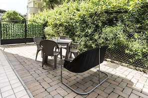 An outdoor seating area with a table and chairs, a black chair, and a metal frame structure.