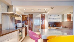 Una cocina moderna con electrodomésticos de acero inoxidable, armarios de madera y una silla de color amarillo brillante.