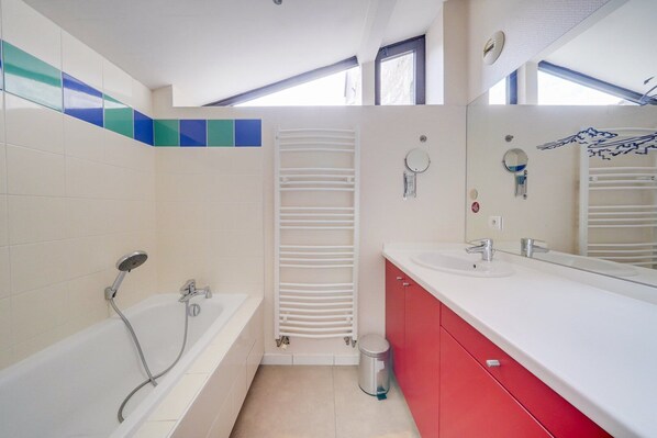 A modern bathroom with a bathtub, a shower, a sink, and a toilet. There is a towel rack and a trash bin.