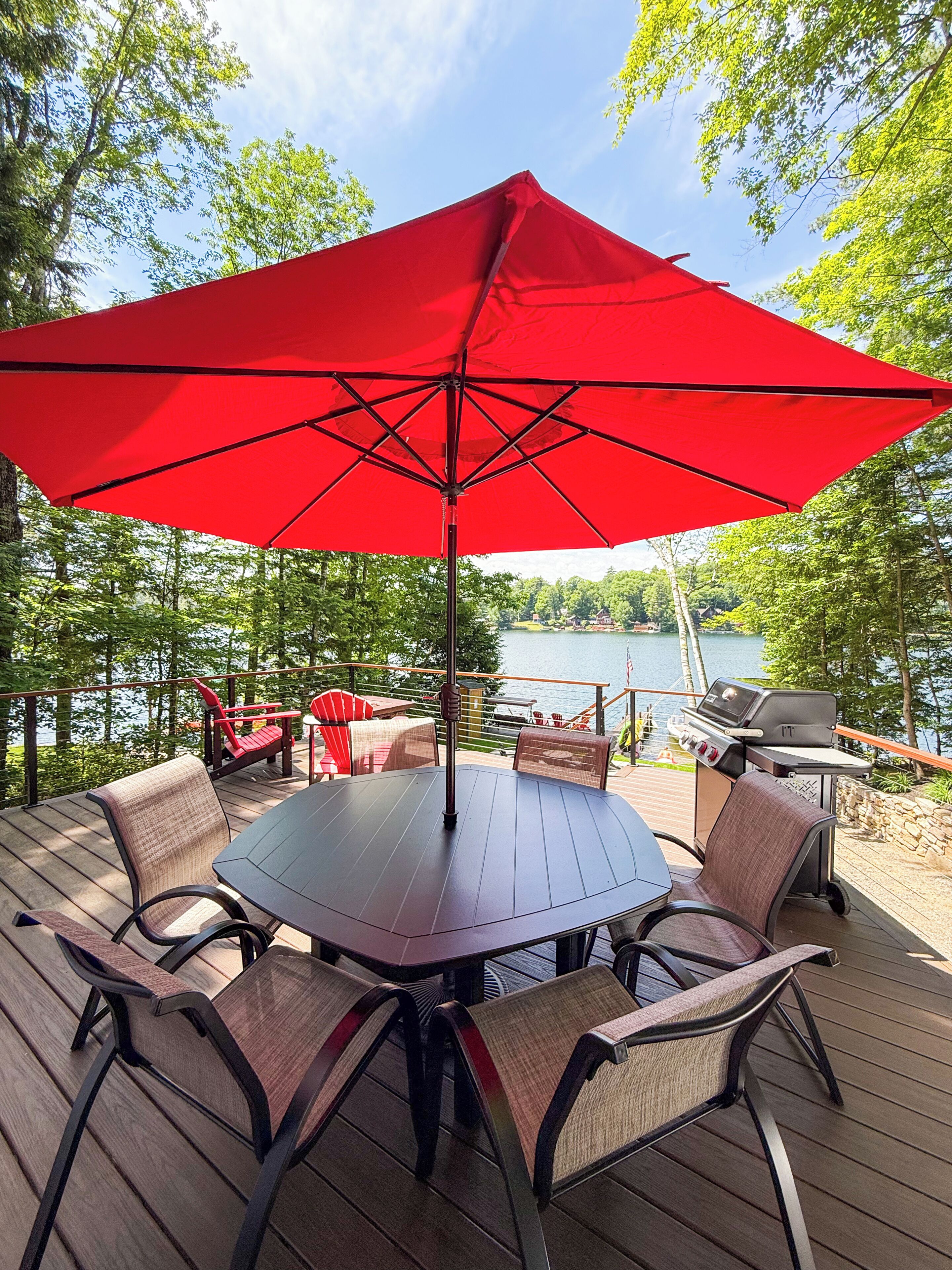 A deck with a table and chairs, a red umbrella, and a grill.