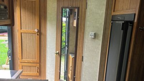Interior compacto de una caravana con una puerta de madera, una pequeña cocina y una zona de estar.