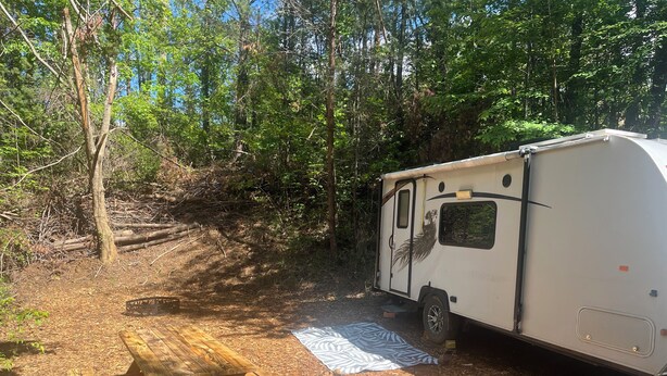 Una caravana blanca estacionada en un área boscosa con una mesa de picnic cerca.