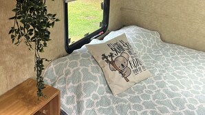 Interior acogedor de una autocaravana con cama, ventana, un mueble de madera y una planta colgante.