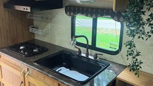 Una cocina compacta con armarios de madera, un microondas integrado, una estufa a gas y un ventanal con vistas al verdor.