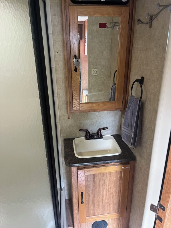 Un baño pequeño con tocador de madera, lavamanos blanco y espejo encima.