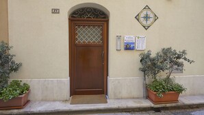 A wooden door with a decorative glass panel, a number plaque, and two informational signs on a beige wall.