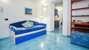 A room with a blue sofa, a framed picture on the wall, and a wooden shelf with items.