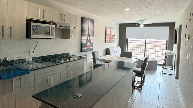 A modern kitchen with a central island, built-in microwave, and stainless steel appliances. There is a dining area with a table and chairs, and a large window offering a view. - Torre Revolución Sutaj Centro (Guadalajara)