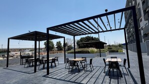 An outdoor patio with tables and chairs, a pergola structure, and a view of a residential area. - Torre Revolución Sutaj Centro (Guadalajara)