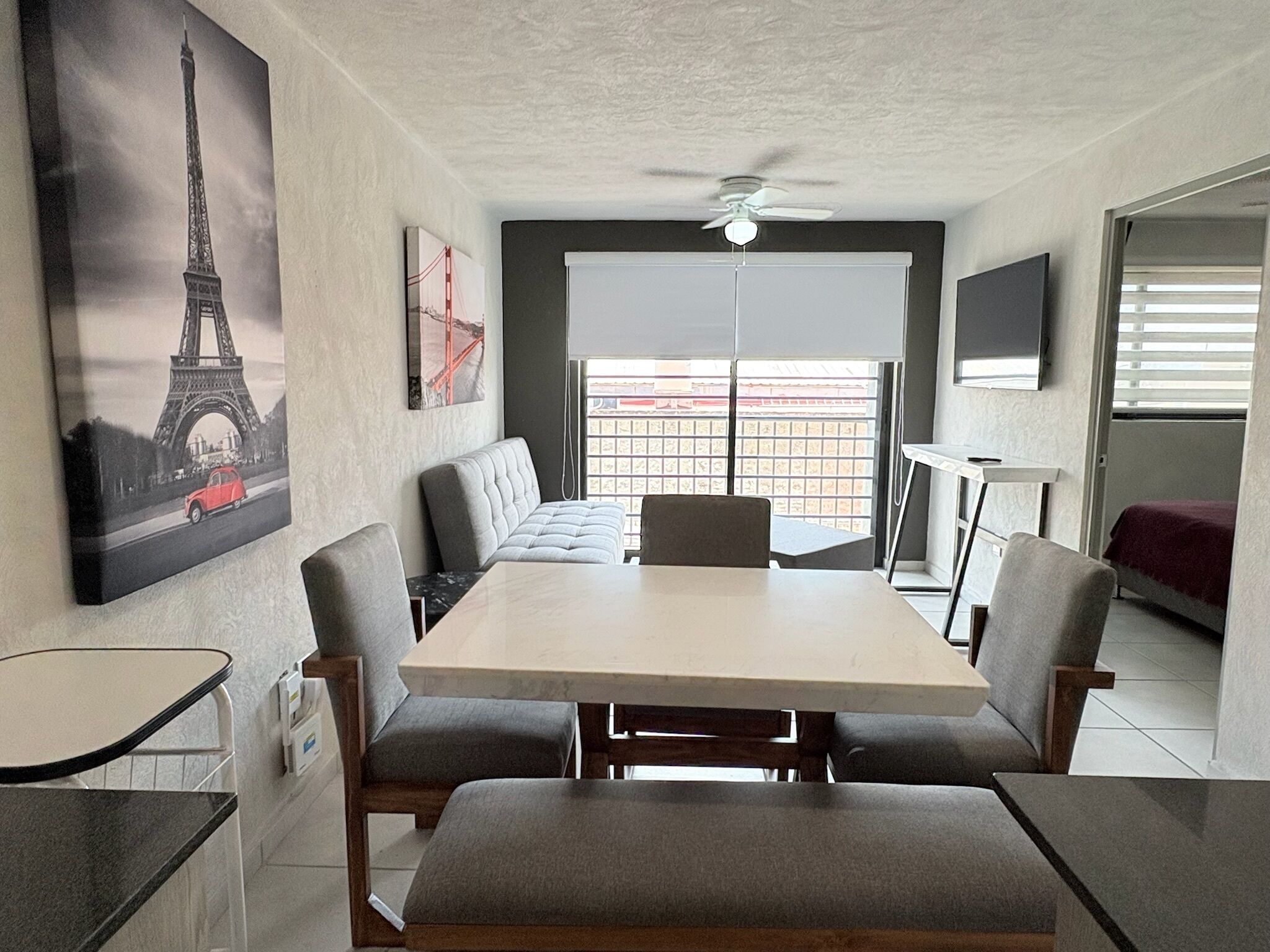 A modern room with a dining table, cushioned seating, a ceiling fan, and artwork of the Eiffel Tower.