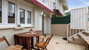 A patio with a wooden table and chairs, a small potted plant, and a staircase leading to an upper level.