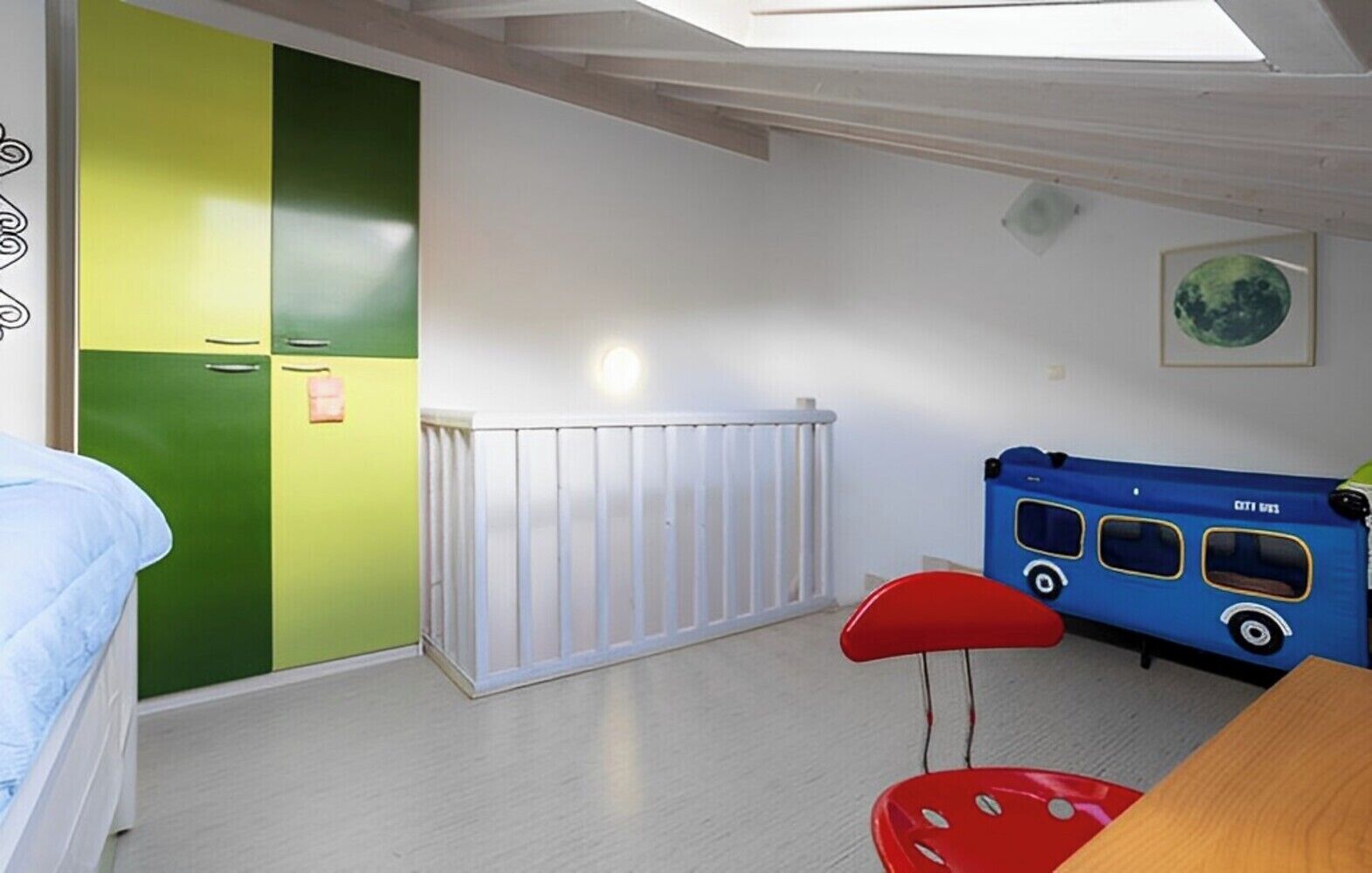 A room with a bunk bed, a green and white wall, a white radiator, a blue playhouse, and a red chair.