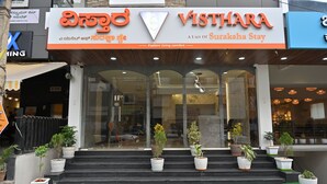 A hotel entrance with a sign reading "Visthara A Unit of Suraksha Stay" and multiple potted plants on the steps. - VISTHARA a unit of Suraksha Stay (Bangalore)