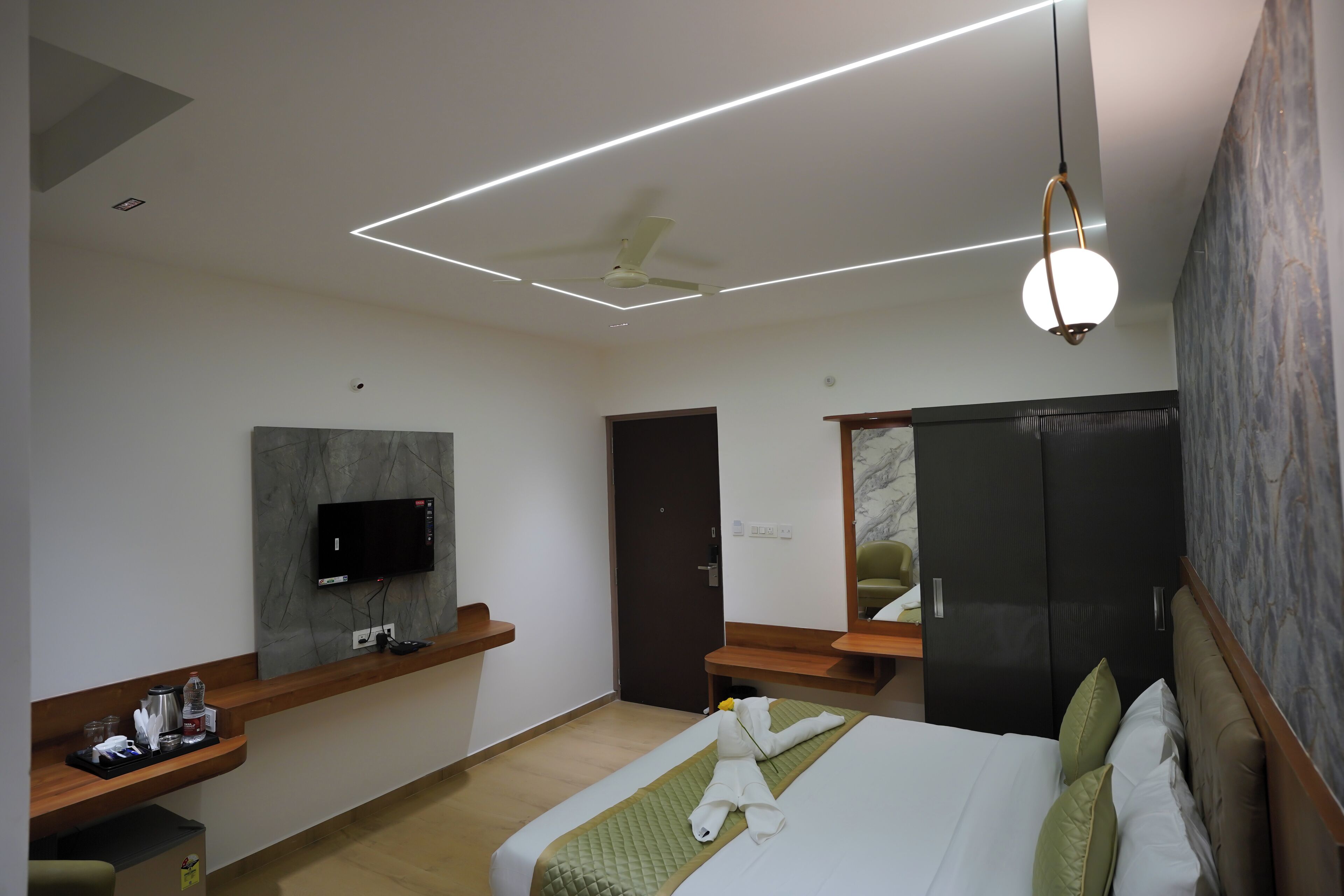 A modern hotel room with a bed, a desk, a flat-screen TV, and a ceiling fan.