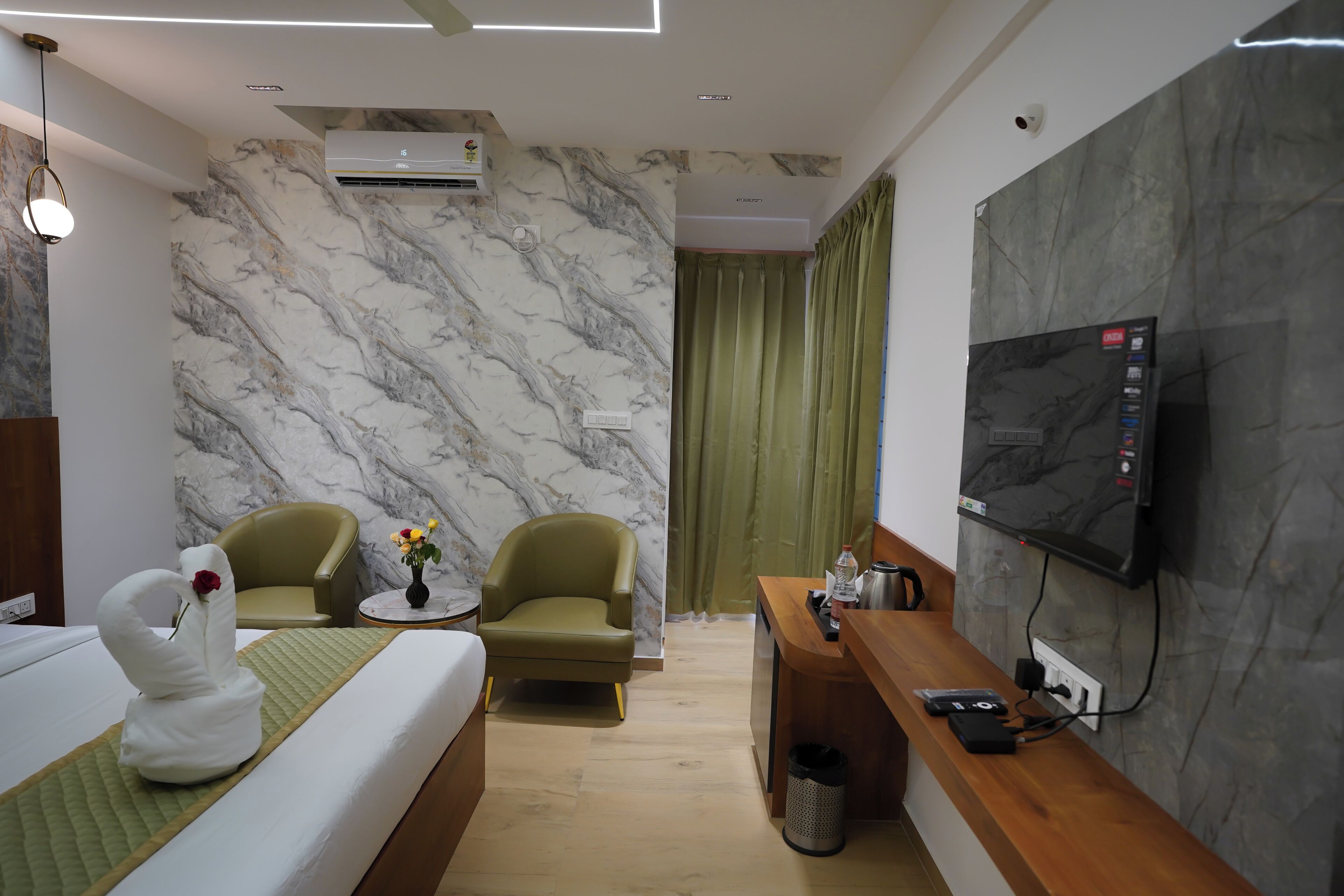 Een hotelkamer met een bed, twee fauteuils, een tafeltje met bloemen, een televisie en een bureau met een prullenbak.