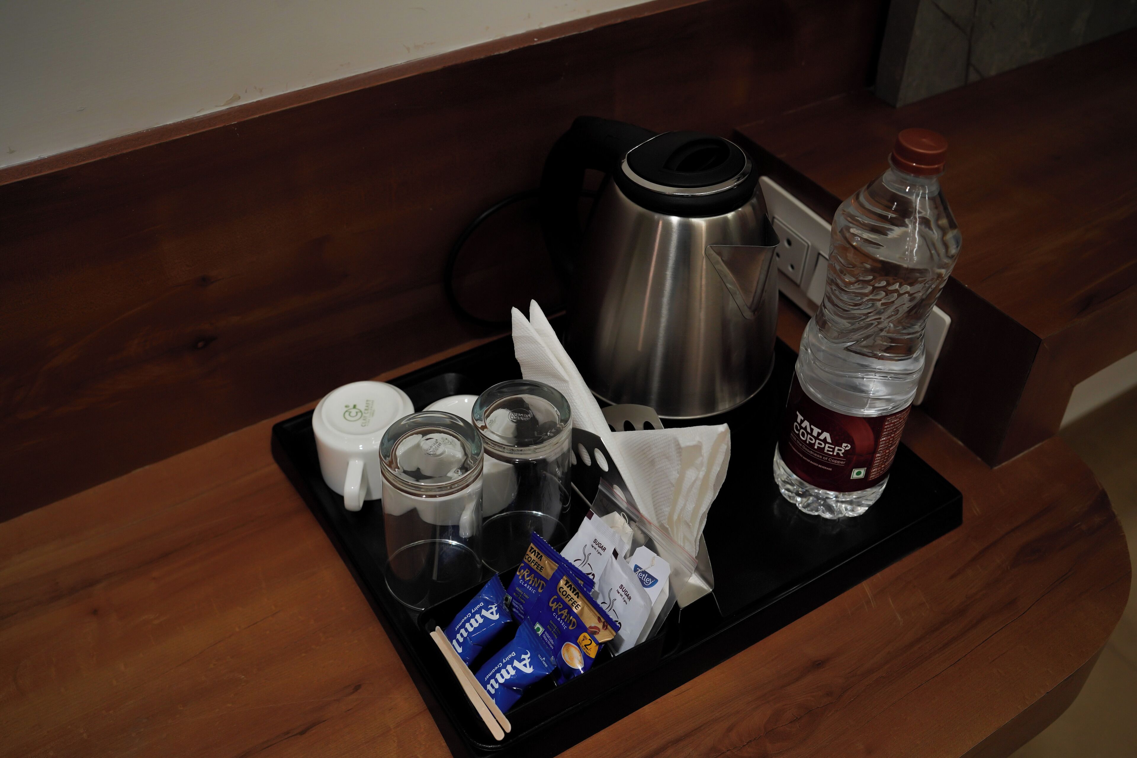 A tray with a coffee maker, a bottle of water, a cup, glasses, and some food packets.