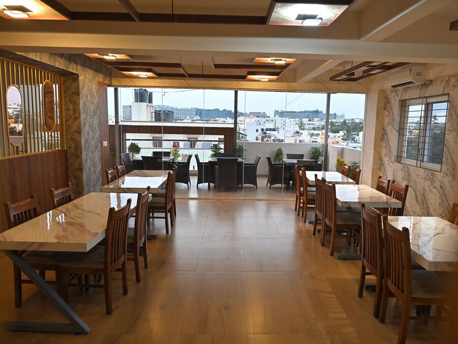 A spacious dining area with marble tables and chairs, large windows offering a city view, and a modern ceiling design.