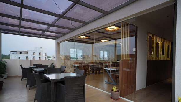 An outdoor patio with glass walls, wicker furniture, and potted plants. - VISTHARA a unit of Suraksha Stay (Bangalore)