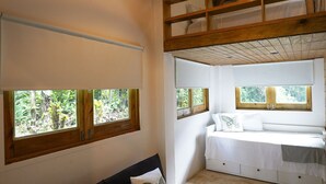 A room with a black sofa, a bed, and a ceiling fan. There are windows with wooden frames and a view of greenery outside. - Indomitable Chalet @ El Yunque Zone (Benítez)