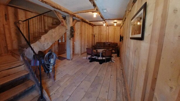 Un interior de madera con una escalera, una zona de comedor con una mesa y sillas, y un cuadro enmarcado en la pared.