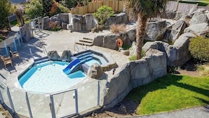 En trädgård med en pool, ett bubbelbad och en stenparti.
