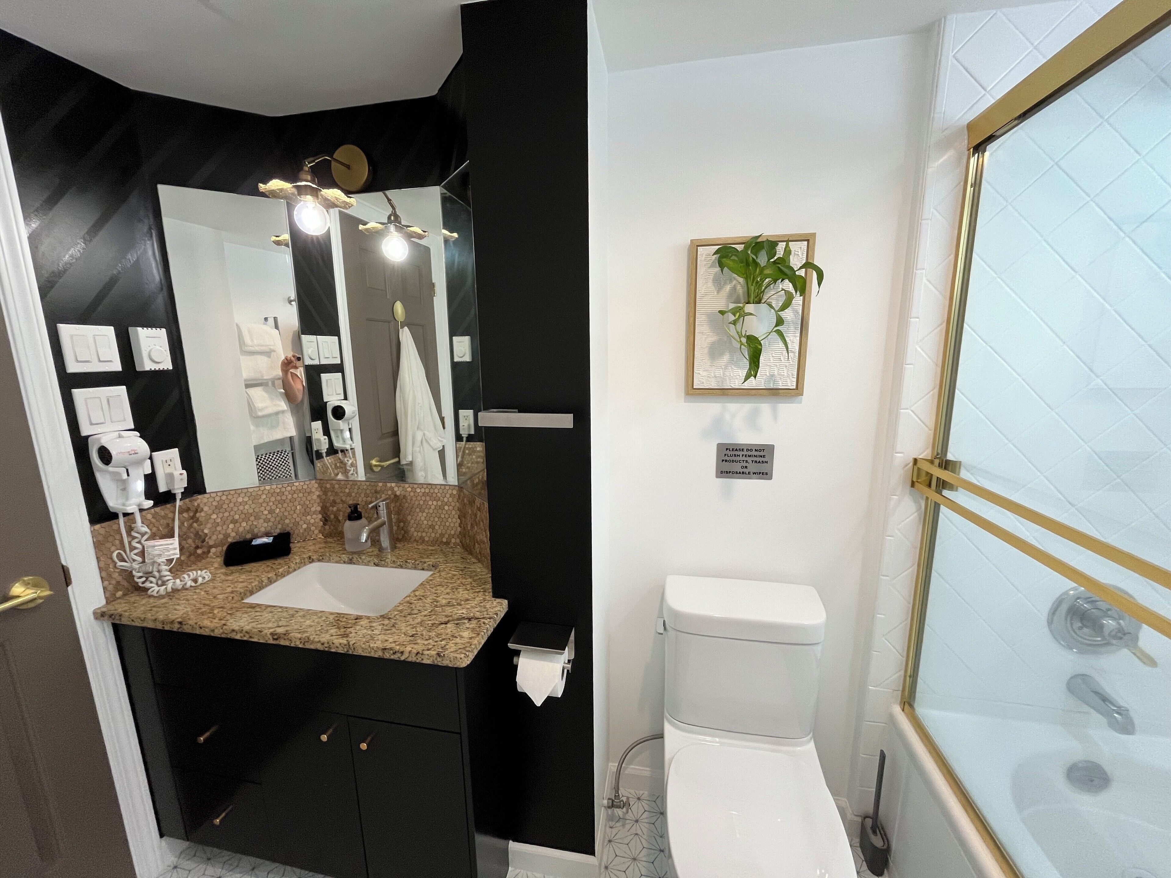 A modern bathroom with a black and white color scheme, a large mirror, a sink, a toilet, and a shower with a glass door.